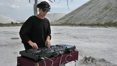 A medium shot of a guy mixing music at a DJ console in the middle of a desert Stock Footage 172315845