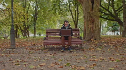 Medium shot of handsome young man working on laptop computer sitting outdoors in Stock Footage 141774644