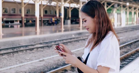 Medium shot of hipster waitng for train in train station, using her phone, Stock Footage 106386816