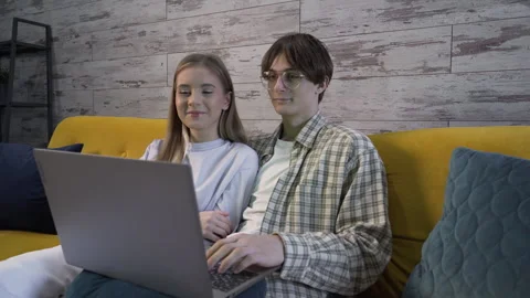 Medium shot Indoors sitting on sofa young couple looking at laptop and talking Stock Footage 258758200
