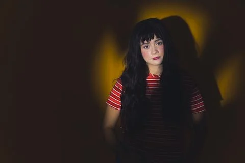 Medium shot of a long dark-haired girl standing in the circle light and looking Stock Photos