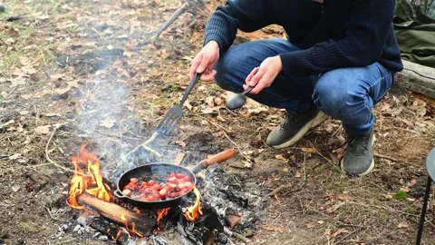 Medium shot of a man cooking cherry tomatoes in a frying pan over a campfire Video stock 334681054