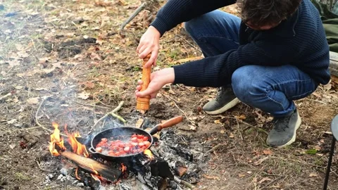 Medium shot of a man cooking cherry tomatoes in a frying pan over a campfire Stockbeeldmateriaal 334681100