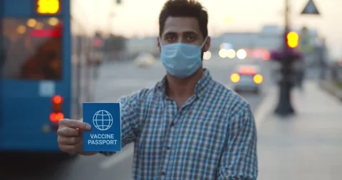 Medium shot of man in mask looking at camera holding vaccine passport outdoors Stock Footage 243631189