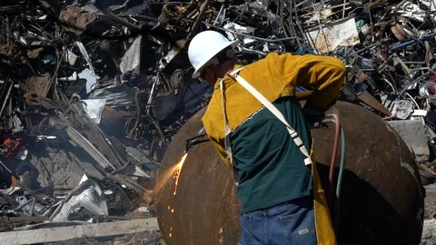 Medium shot of a man torch cutting large scrap metal in junkyard in slow motion Stock Footage 100836086