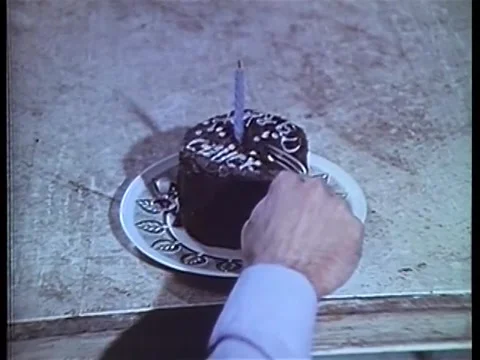 Medium shot of man trying to cut small birthday cake with difficulty, 1970s 스톡 동영상 58858737