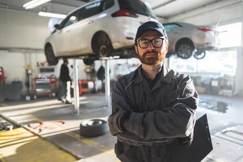 Medium shot of a mechanic standing hands-crossed holding car notes and looking Stock Photos