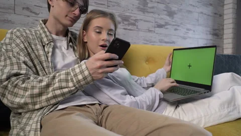 Medium shot a modern young couple is sitting on the couch and using gadgets Stock-Footage 259333632
