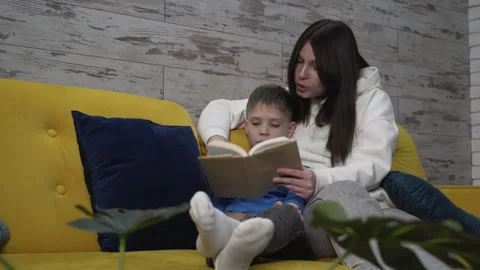Medium shot mom and son sitting on the couch reading a book Stock Footage 256981476