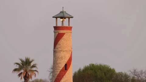 Medium shot of old brick lighthouse with trees and palm tree Video stock 172205930