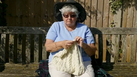 Medium shot of an old lady sitting on a bench, knitting. Stock Footage 76251624