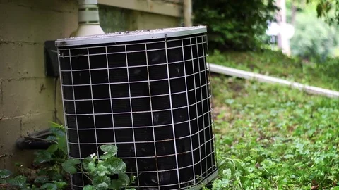 Medium shot of old rusty air conditioner amongst weedy area beside a ranch home Stock Footage 75872288