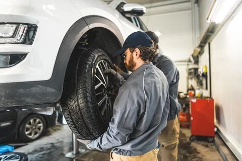 Medium shot of one mechanic replacing a car tyre and other one helping him Foto stock