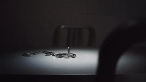Medium shot of a pair of handcuffs in an interrogation room. An out of Video stock 99897317