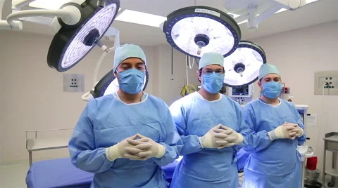 MEDIUM SHOT-PAN RIGHT. Three surgeons ready for surgery posing for the camera. Stock Footage 48946055