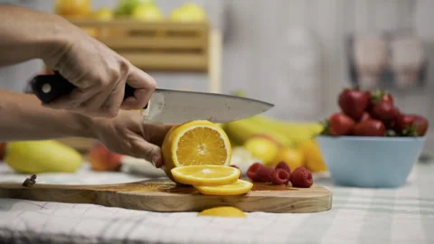 Medium shot of person using knife to slice through orange on counter with other Stock Footage 341233126