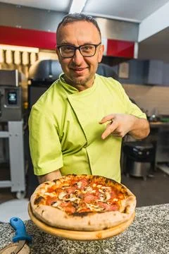 Medium shot of a professional chef pointing at the pizza on a wooden board Stock Photos