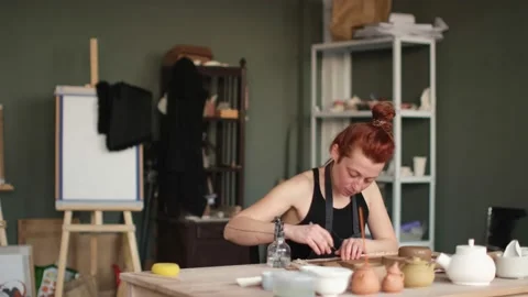 Medium shot of redhead ceramic artist cut clay for ceramic teapot Stock Footage 236373114