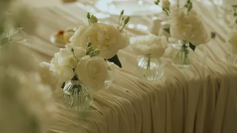 Medium shot of a row of small glass vases filled with fresh white roses and 库存影片 340920513
