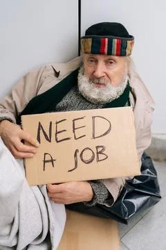 Medium shot of sad despair elderly homeless man with sign seeking employment on Stock Photos