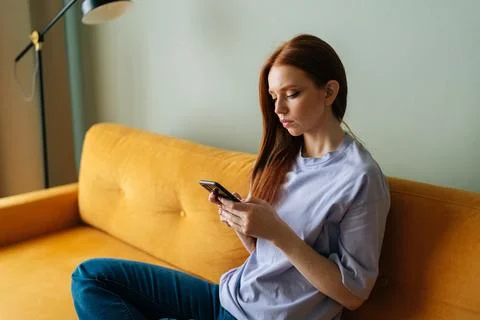 Medium shot of sad red-haired young woman looking at smartphone screen received Stock Photos