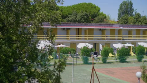 Medium shot of seaside motel with trees and tennis court in front of guest rooms Stock Footage 313783625