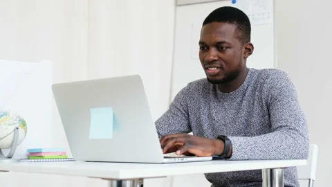Medium shot smiling young African programmer using laptop at workplace in modern Stock Footage 109156455