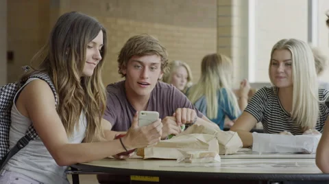 Medium shot of students examining cell phone in school cafeteria / Mapleton, Stock Footage 68218127