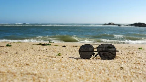 Medium shot of sunglasses on sandy beach as waves break in background Stock Footage 108642546