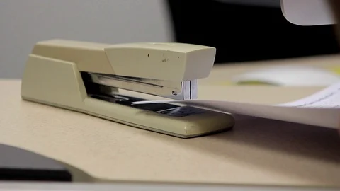 A medium shot of a tan office stapler being used to staple papers in an office 動画素材 88487874
