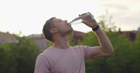 Medium shot of thirsty young man drinking water in plastic bottle outdoors. Stock Footage 157971174