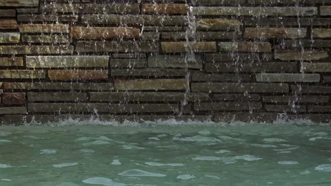 Medium shot water pouring down stone wall into pool 스톡 동영상 76256476