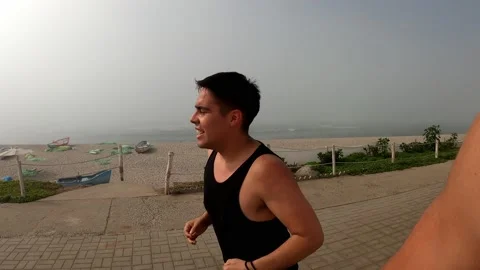 Medium shot of a white man with a black sleeveless shirt running along the beach Vidéo 194444706