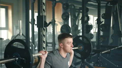 Medium shot of young athlete performing barbell squats in fully-equipped gym Stock Footage 241588818