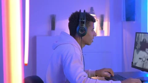 Medium shot of young black gammer in headphones playing in online shooter Video stock 130656893
