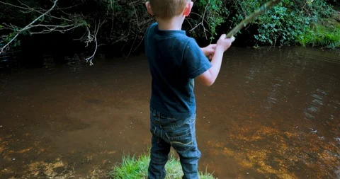 Medium shot young boy playing with stick in river Stock Footage