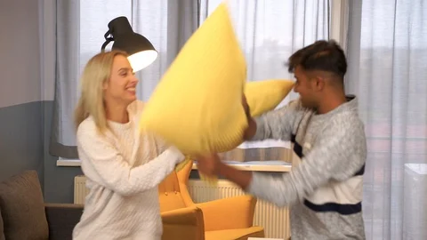 Medium shot of a young interracial couple having a pillow fight at living room. Stock Footage 119301624