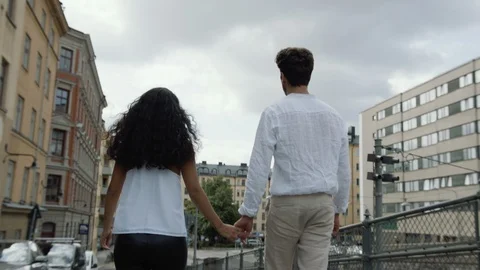 Medium shot of a young man and woman walking hand in hand on a street. Video stock 116005890