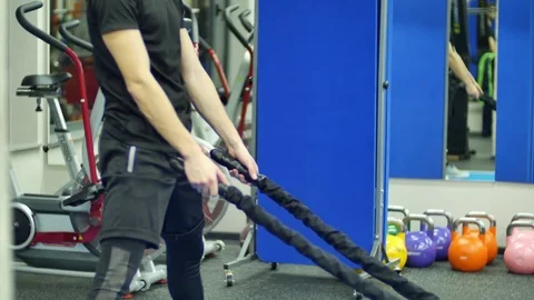 Medium shot young man exercising arms and shoulders with rope in gym Stock Footage 72436742