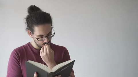 Medium shot of young man reading a book and biting his nails Stock Footage 161551941