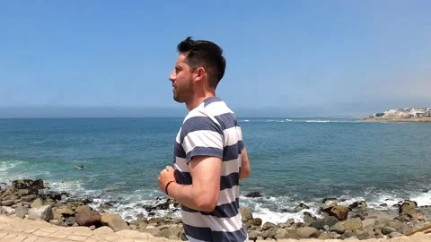 Medium shot of a young white man running along a beautiful colorful beach with Stock Footage 195134120