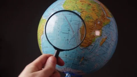 Medium-sized globe with human hands looking with a magnifying glass on a black Stock Footage 75002459
