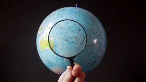 Medium-sized globe with human hands looking with a magnifying glass on a black Stock Footage 75010300