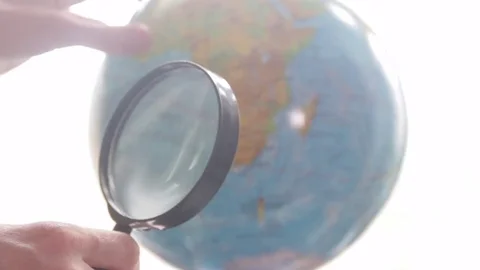 Medium-sized globe with human hands looking with a magnifying glass on a black Stock Footage 75187650