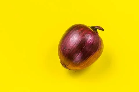 A medium-sized, red, shiny onion sits on a yellow background. Flat lay Stock Photos
