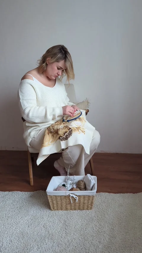 Medium-sized woman in light clothes embroiders a picture in gold and beige .. Stock Footage 264775002