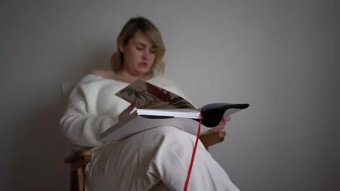 A medium-sized woman in light clothes reads a book while sitting in a white.. Stock Footage 264775101
