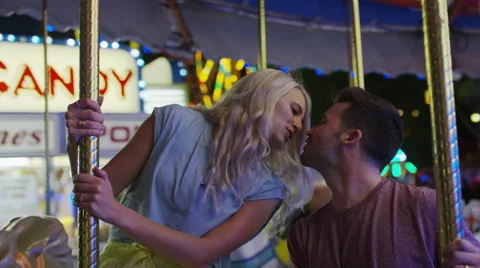 Medium slow motion low angle shot of couple kissing on carousel / Pleasant Vídeo Stock 68218005