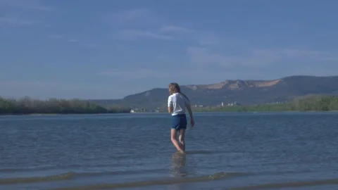 Medium Static Shot of Girl Picking Up Rock and Throwing It into Danube River Stock Footage 346500629