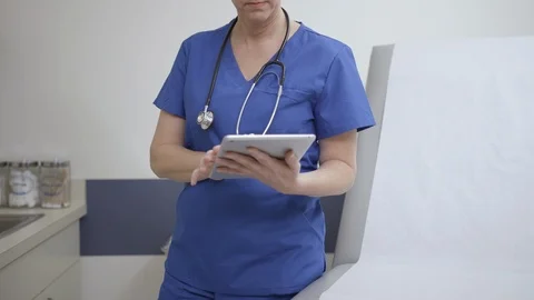 Medium, tilting shot of nurse reading and typing on iPad or tablet in exam room Stock Footage 109507833